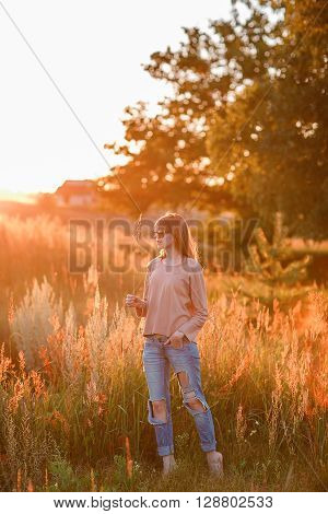 Portrait of young modern girl on the background of nature. Young woman  on a background sunset. Young woman in ripped jeans. in sun glasses