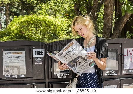 Vail, USA - September 10, 2015: Blonde young woman focused reading the local newspaper by a stand in Vail, Colorado