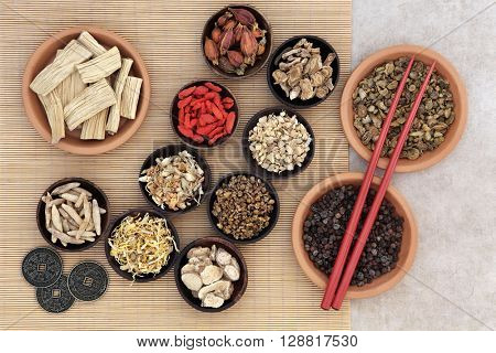 Traditional chinese herbal medicine with herb selection, i ching coins and chopsticks over bamboo background.