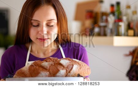 Young woman holding tasty fresh bread in her kitchen .