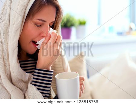 Portrait of a sick woman blowing her nose while sitting on the sofa.