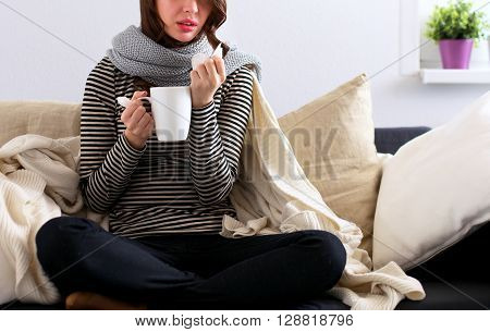 Portrait of a sick woman blowing her nose while sitting on the sofa.