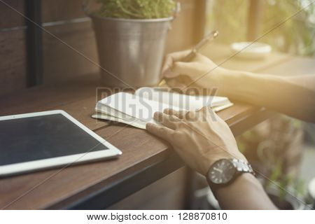 Man Writing On Notebook With Digital Tablet