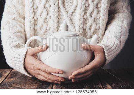 Adult Woman Hands Hug Big Ceramic Teapot With Hot Drink Inside. Close Up, Wearing Cozy Warm Sweater,