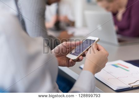 close up of  businesswoman hands  using smart phone, people group in office meeting  room blurred in backgronud