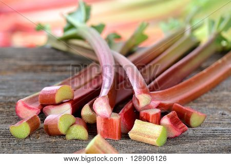 Fresh rhubarb on a wooden table, in the background other rhubarb stems in soft focus