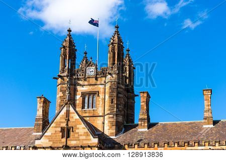 Sydney Uni building facade with Australian flag. University of Sydney against deep blue sky with white clouds daytime photo