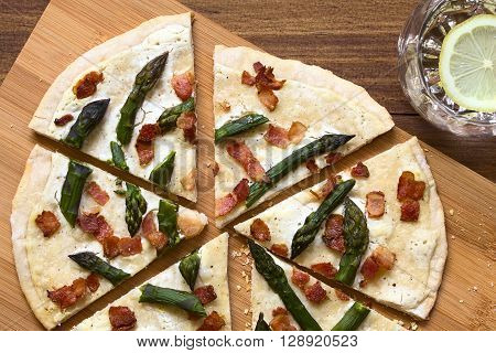 Green asparagus and bacon tarte flambee or Flammkuchen a typical Alsatian and South German dish photographed overhead on wooden board with natural light