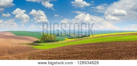 Big panoramic view of beautiful spring hills landscape with colorful fields, sunny day sky