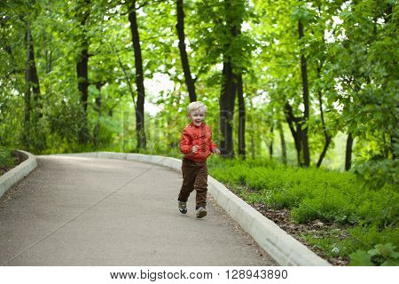 Portrait in full growth, Happy Little boy in orange jacket walking in summer park