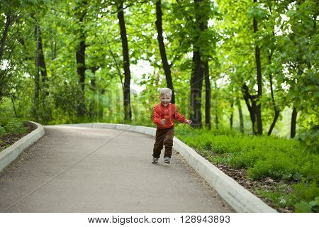 Portrait in full growth, Happy Little boy in orange jacket walking in summer park