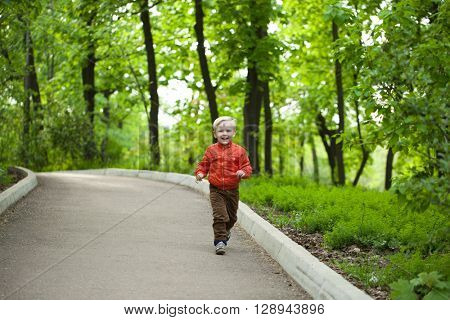 Portrait in full growth, Happy Little boy in orange jacket walking in summer park