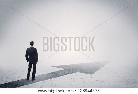 A professional businessman thinking while standing on a black arrow pointing forward in grey space concept
