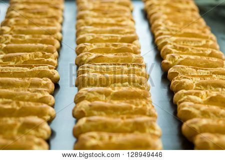 Long rows of eclair shells. Eclairs on wide conveyor belt. Each one has perfect shape. Company's standards of production.