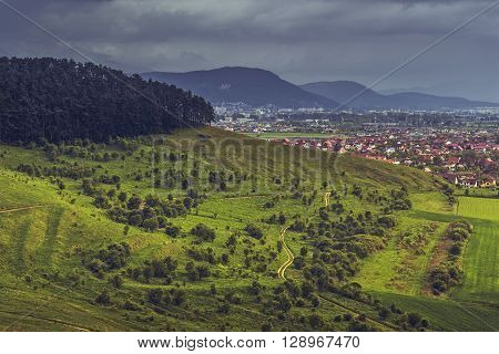 Spring overcast scenery with a wide green meadow opening with trails on Lempes hill near Sanpetru city Brasov county in Transylvania region Romania.