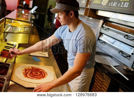 Handsome pizzaiolo making pizza at kitchen in pizzeria.
