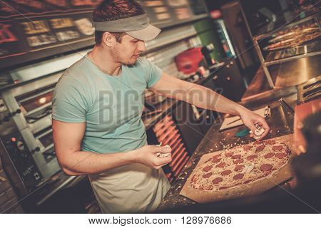 Handsome pizzaiolo making pizza at kitchen in pizzeria.