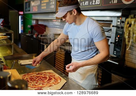 Handsome pizzaiolo making pizza at kitchen in pizzeria.