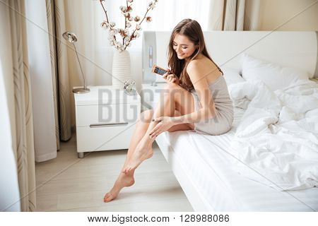 Charming woman applying cream on legs on the bed at home