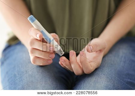 Diabetic woman taking blood sample with lancet pen, closeup