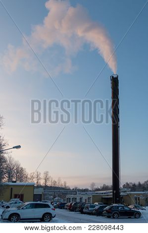 High Chimney With Smoke And A Clear Blue Sky. Overlooking A Carpark Infront Of A Hospital In Sweden