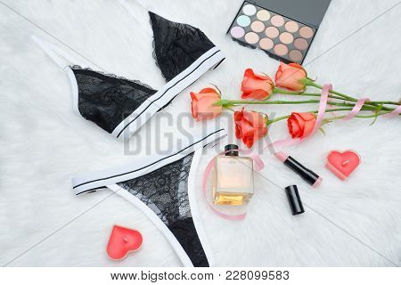 Black Set Of Lacy Underwear On White Fur. Orange Roses, Eye Shadows, Lipstick And Candles. Fashionab
