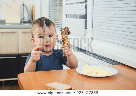 Baby In Kitchen Hands Holding And Showing Chicken Meat In One Hand And Fork In The Other