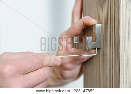 A Man Is Installing A Hook For Clothes. He Is Using A Hex Key To Fix The Bracket Of The Hook.
