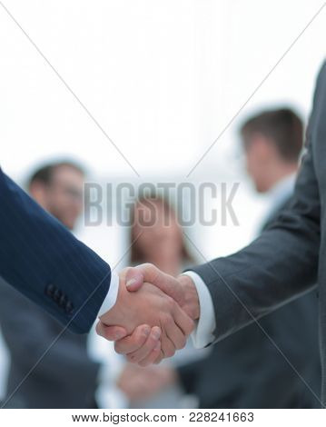 Two businessmen shaking hands with colleagues  on background.