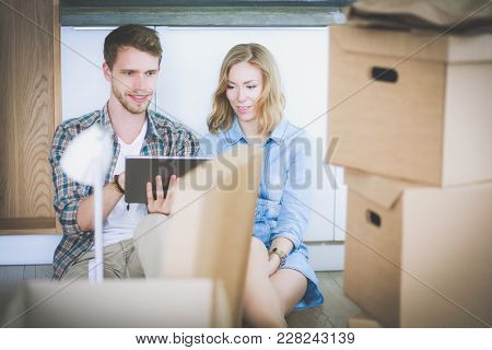 Young couple moving in new home.Sitting and relaxing after unpacking.Looking something on laptop. Young couple