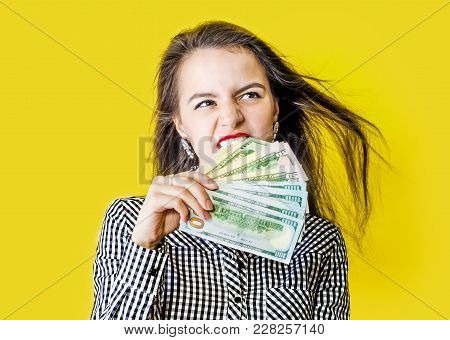 Beautiful Young Woman Eats Cash, Yellow Background