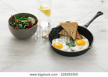 Breakfast Table. Fried Egg In Frying Pan, Salad, Lemon Water