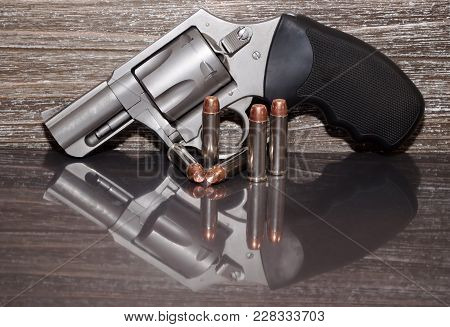 A Stainless Steel 357 Magnum Revolver With Five Bullets In Front Of It With A Wooden Background And 