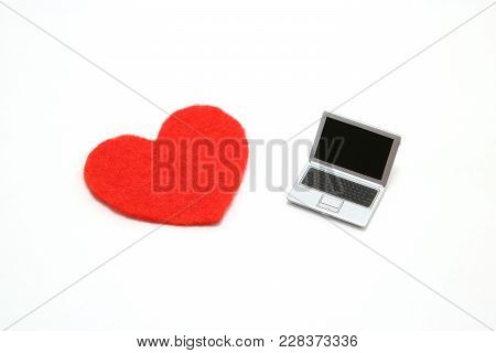 Miniature laptop and a red heart on white background.
Concept of love using a personal computer.