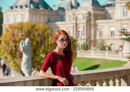Young Redhead Woman In Sunglasses And Red Dress Resting Near Stairs