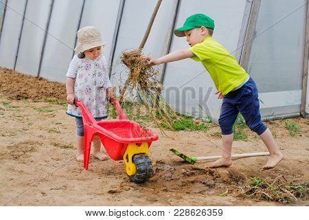 Children Work In The Garden With A Shovel And A Wheelbarrow