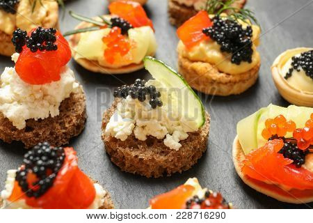 Delicious canapes with black caviar on dark background, closeup