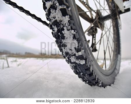 Rear Wheel Detail Of Mtb. Snow Flakes Melting On Dark Off Road Tyre. Winter Weather In The Field.