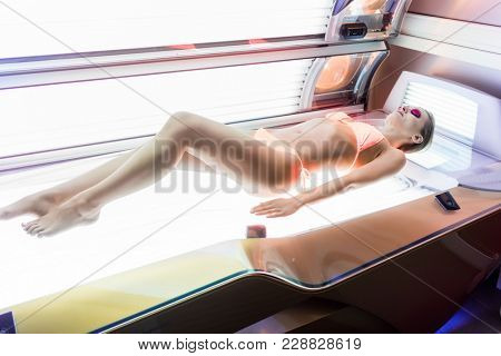 Beautiful woman wearing protective goggles and swimsuit while lying down on an horizontal bed for indoor tanning in a modern beauty salon