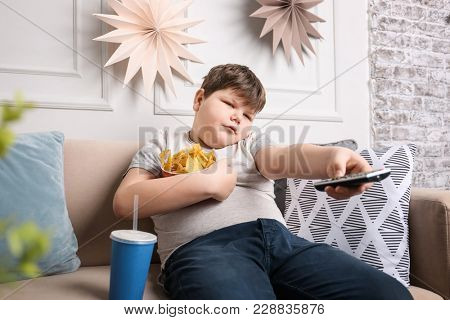 Overweight boy watching TV with snacks indoors