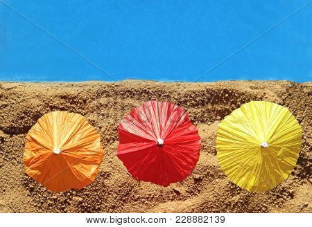 Row Of Three Colorful Parasols At The Beach, In The Sand, Blue Water, Top View