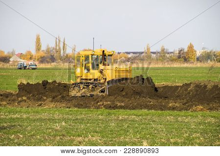 The Yellow Tractor With Attached Grederom Makes Ground Leveling. Work On The Drainage System In The 