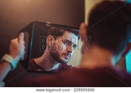Portrait Of A Young Bearded Guy Who Looks At Himself Through The Mirror In The Beauty Salon.