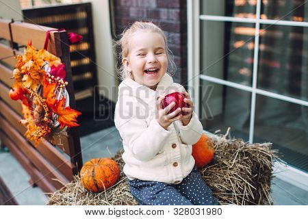 Adorable Laughing Caucasian Baby Toddler In White Knittes Jacket Sitting On The Haystack With Pumpki
