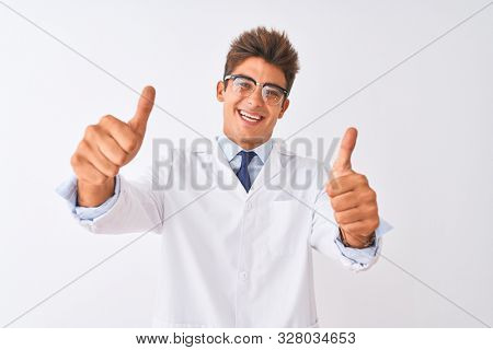 Young handsome sciencist man wearing glasses and coat over isolated white background approving doing positive gesture with hand, thumbs up smiling and happy for success. Winner gesture.