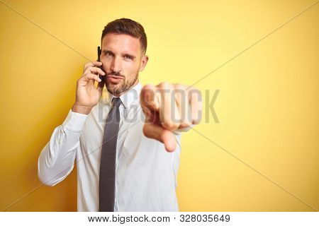 Young handsome business man talking on the phone over yellow isolated background pointing with finger to the camera and to you, hand sign, positive and confident gesture from the front