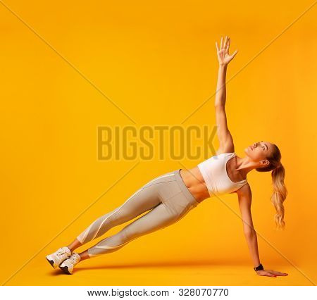 Sporty Girl Doing Side Plank Exercise During Workout Over Yellow Background. Studio Shot