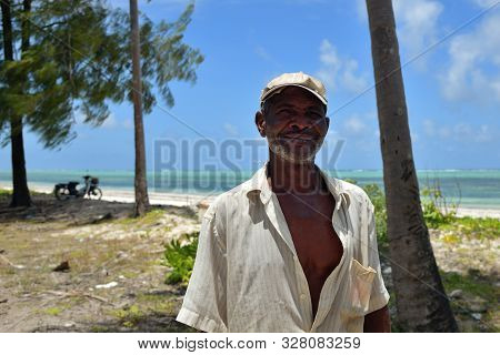Pingwe, Zanzibar - October 6, 2019: Portrait Of The Old Local Fisherman, Blue Ocean And Palms Tree O