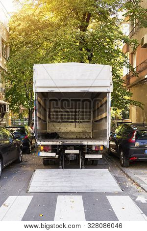 Open Furniture Delivery Truck On A City Street. Empty Moving Van With Rear Doors Opened. On An Autum