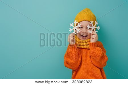 Winter portrait of happy child wearing knitted hat, snood and sweater. Girl having fun, playing and laughing on teal background. Fashion concept.                               